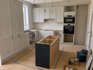 Shaker kitchen installation in Dublin showing island positioning, cabinetry fitting and integrated oven housing.