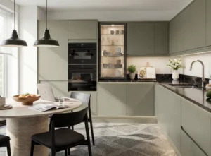 L-shaped kitchen layout in Dublin home with reed green cabinets, built-in ovens, glass display cabinet, black worktops and dining area