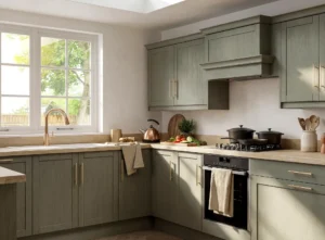L-shaped kitchen layout in Dublin home with reed green cabinets, brass handles, corner worktops, window sink and built-in hob