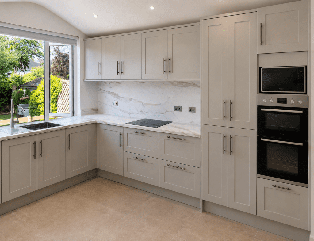 Light neutral Shaker kitchen in Malahide, Dublin with marble-effect laminate worktops, tall storage cabinets and integrated ovens.