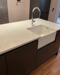 White Belfast sink and chrome tap set into a quartz worktop on a graphite handleless kitchen island in Rathfarnham, Dublin