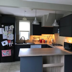 Graphite handleless kitchen with an oak-effect breakfast bar, black appliances and warm under-cabinet lighting in a Drumcondra, Dublin home