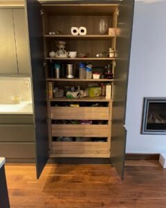 Open tall pantry cupboard with oak-effect shelves and internal drawers in a graphite handleless kitchen in Rathfarnham, Dublin