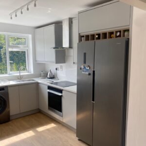 Freestanding fridge-freezer integrated beneath closed overhead cabinetry and open wood-grain shelving in a light grey kitchen