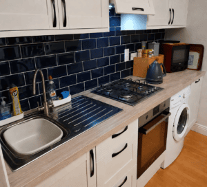 Stainless steel sink and built-in gas hob set into the oak-effect laminate worktop against navy metro wall tiles