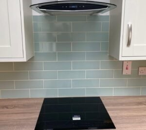 Black glass induction hob set into a laminate worktop beneath a pale grey-green subway tile splashback