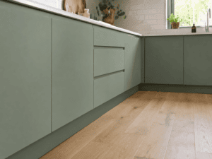Sage green kitchen plinth fitted beneath handleless base cabinets with light wood flooring in an Irish home
