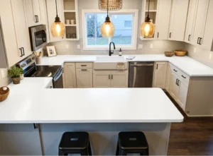 Snow white laminate worktops in a U-shaped Shaker kitchen with a breakfast bar, farmhouse sink and black handles in an Irish home.