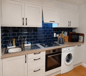 Close view of white Shaker cabinet doors with black curved handles above a continuous oak-effect laminate worktop