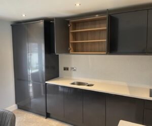 Open wall cabinet with light oak-effect shelving above a sink in a gloss graphite handleless kitchen