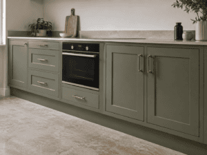 Sage green base kitchen presses with Shaker doors, brass handles and a built-in oven