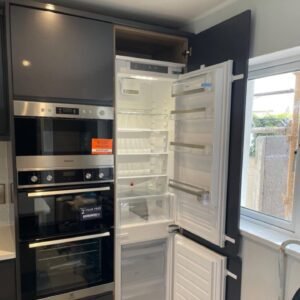Tall appliance housing with stacked built-in cooking appliances and an integrated fridge-freezer hidden behind a matching graphite door