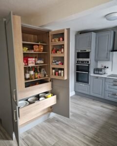 Open tall larder unit in a Dust Grey shaker kitchen in Raheny, Dublin, showing shelving and pull-out drawers