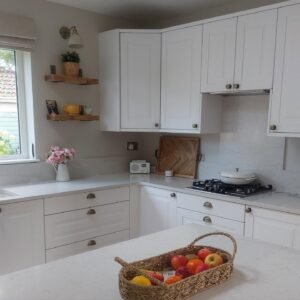 Porcelain Shaker kitchen in Clontarf, Dublin, with white cabinets, antique brass handles, a gas hob and a fruit basket on the island.