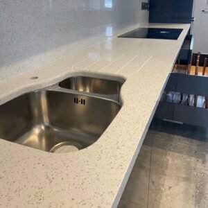 Undermount sink with drainage grooves cut directly into a light-flecked quartz worktop