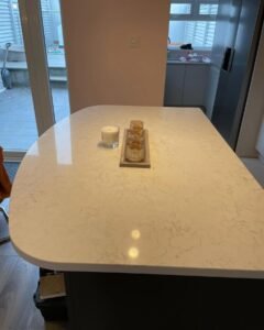 Graphite island with rounded corners in front of a separate window sink zone and freestanding fridge-freezer in a Sutton kitchen