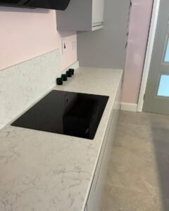 Black glass hob set into a light grey marble-effect quartz worktop with a partial splashback in a Sutton kitchen