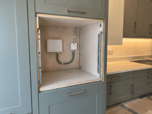 Empty tall cabinet prepared for a built-in oven, showing the electrical connection point, isolator switch and conduit.