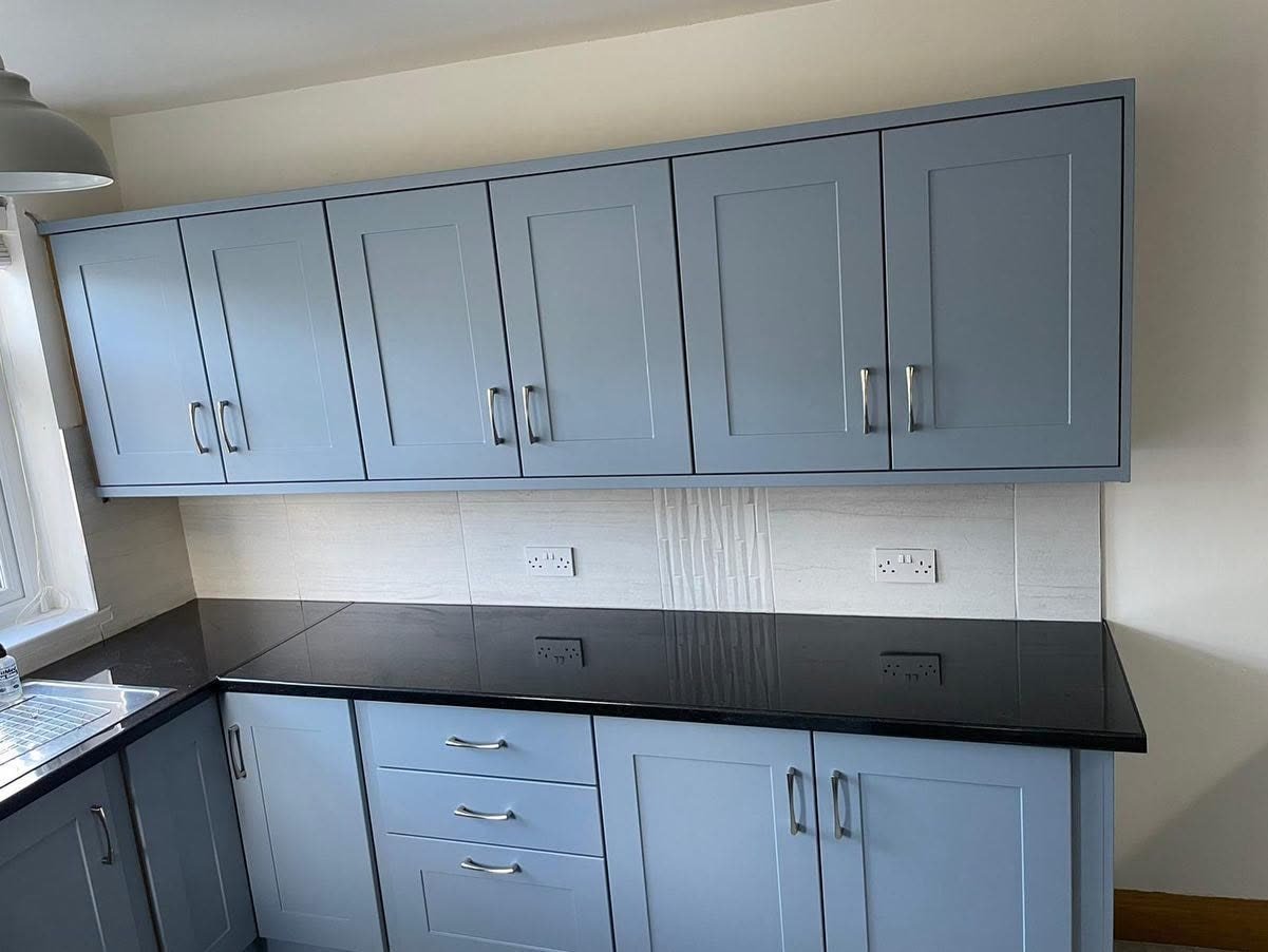 Row of Denim blue-grey shaker wall cupboards above a dark speckled worktop and pale tiles with a vertical feature tile strip