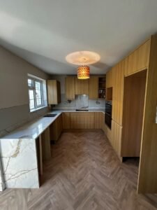 U-shaped natural oak slab kitchen in Clontarf with a white quartz waterfall worktop, tall units to the ceiling and a herringbone floor