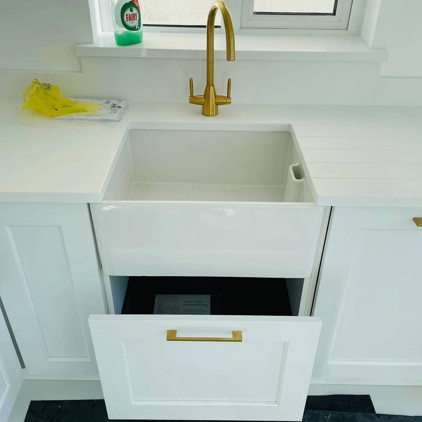 White Belfast butler sink with a brushed brass twin-lever tap and drainer grooves cut into a white quartz worktop