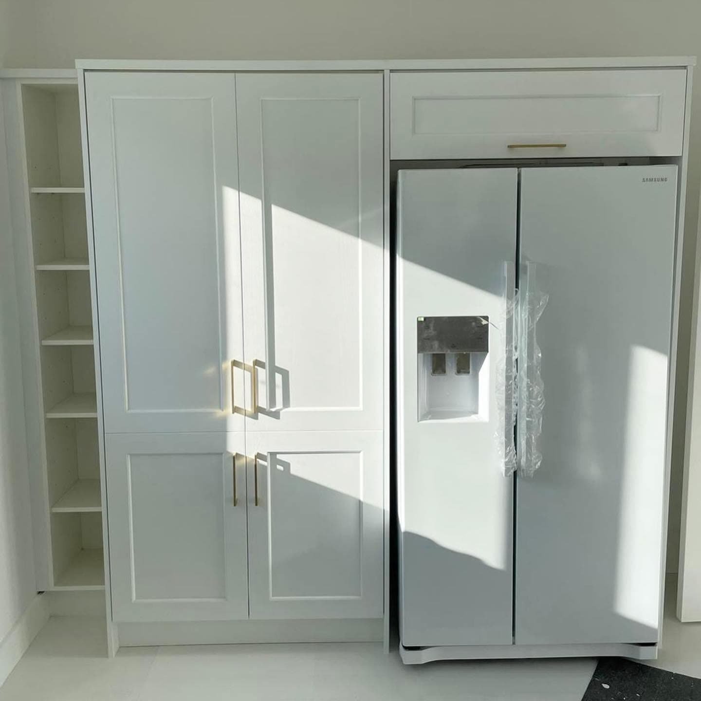 White shaker pantry cupboards and open end shelves beside a Samsung side-by-side fridge in a tall housing