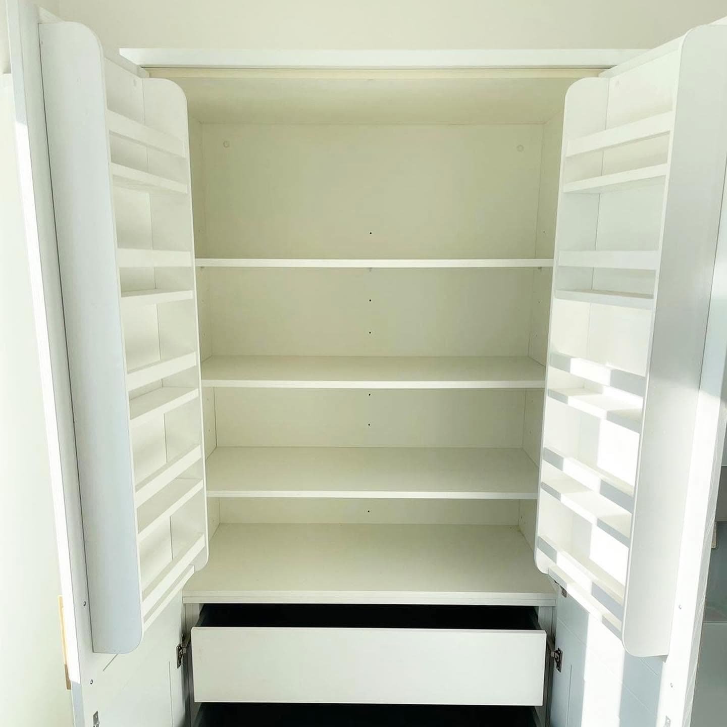 Inside a white double-door pantry larder with racks on both doors, adjustable shelves and an internal drawer
