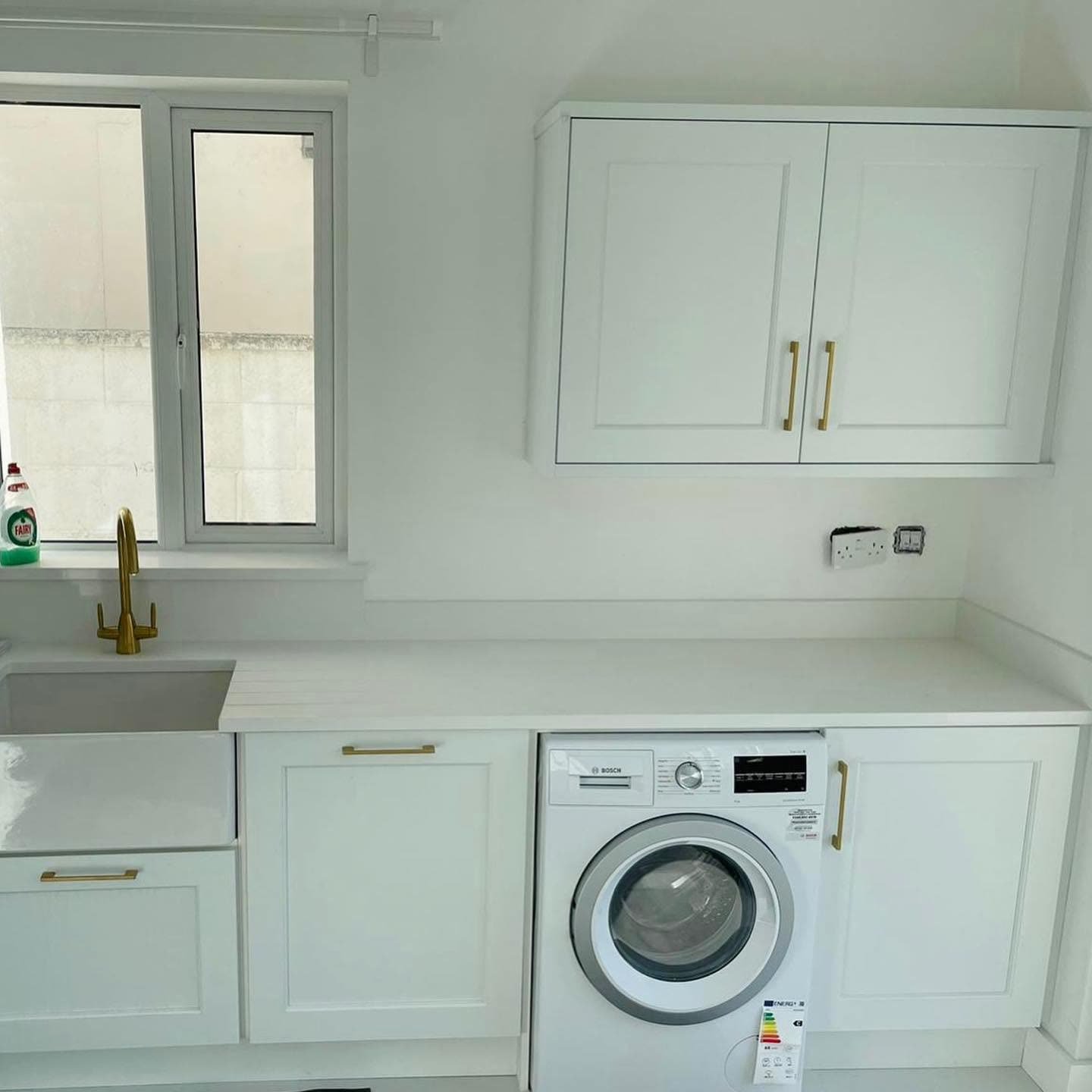 Bosch washing machine built in under a white quartz worktop between white shaker base units, with a wall cupboard above